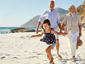 Happy couple enjoying a walk on the beach with their young granddaughter.